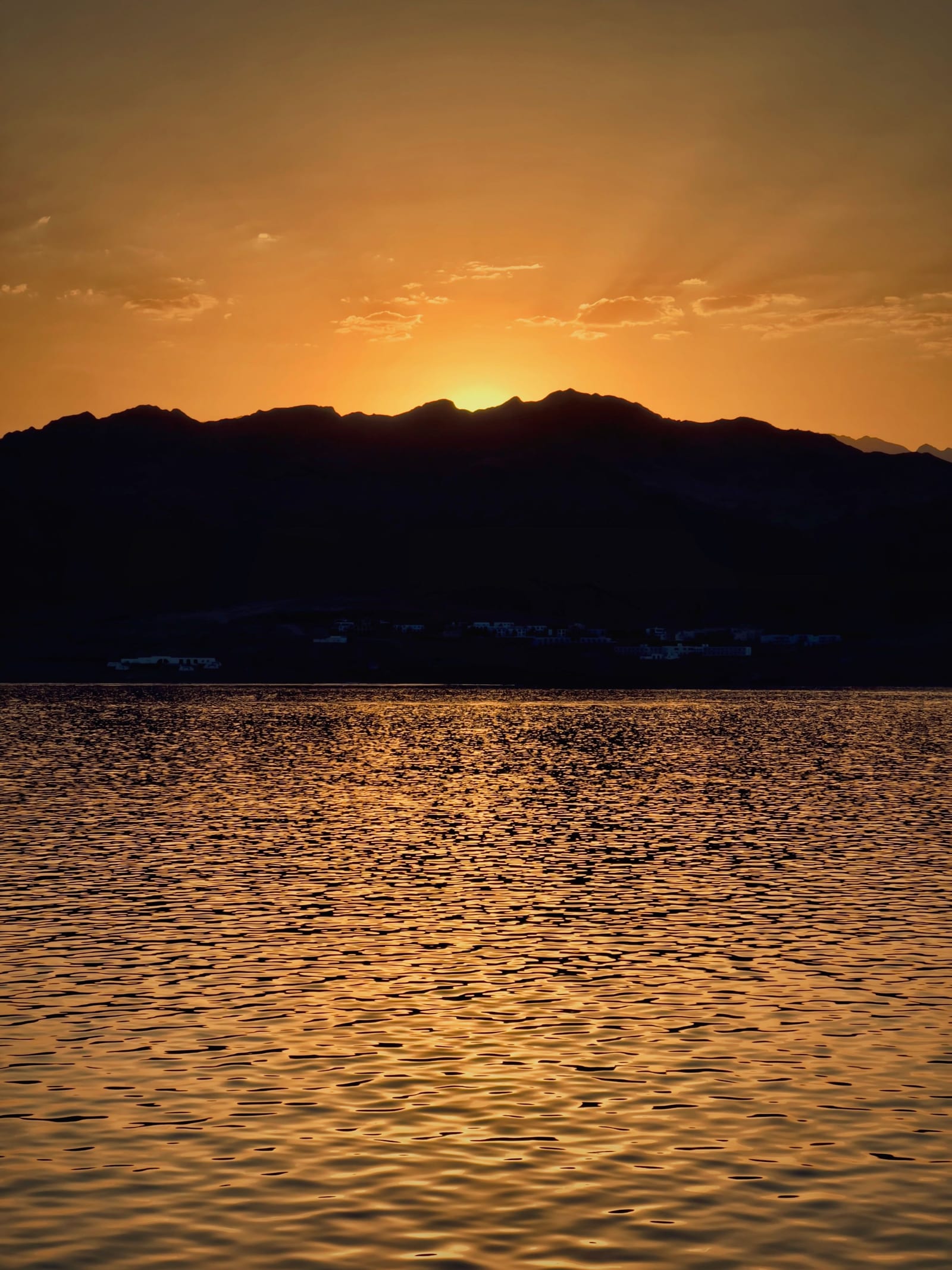 Kızıldeniz kıyısında gün batımı: dağ siluetleri, deniz ve uzakta kıyı boyunca uzanan resort şeridi